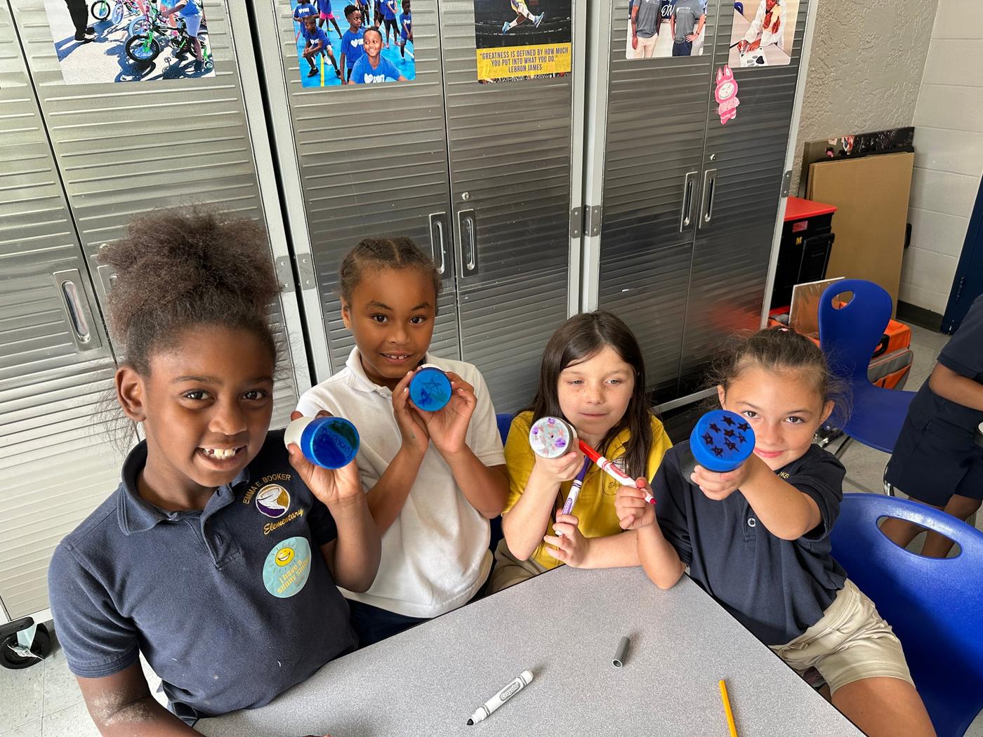 Four students show off instruments they decorated with markers.