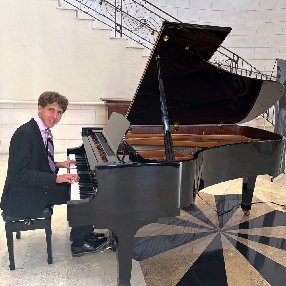 Jack Greenwell seated at a grand piano, smiling at the camera.