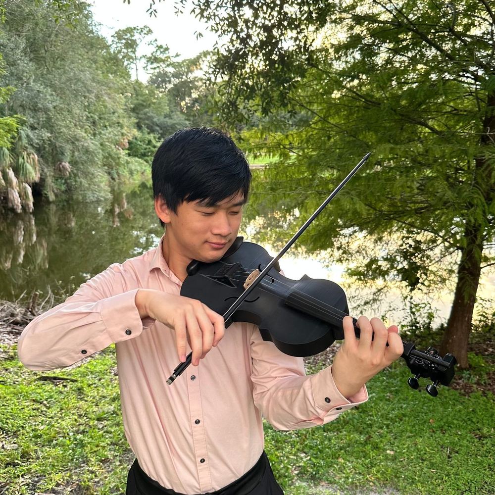 Jeremy Hu playing a 3D-printed violin outdoors beside a pond.