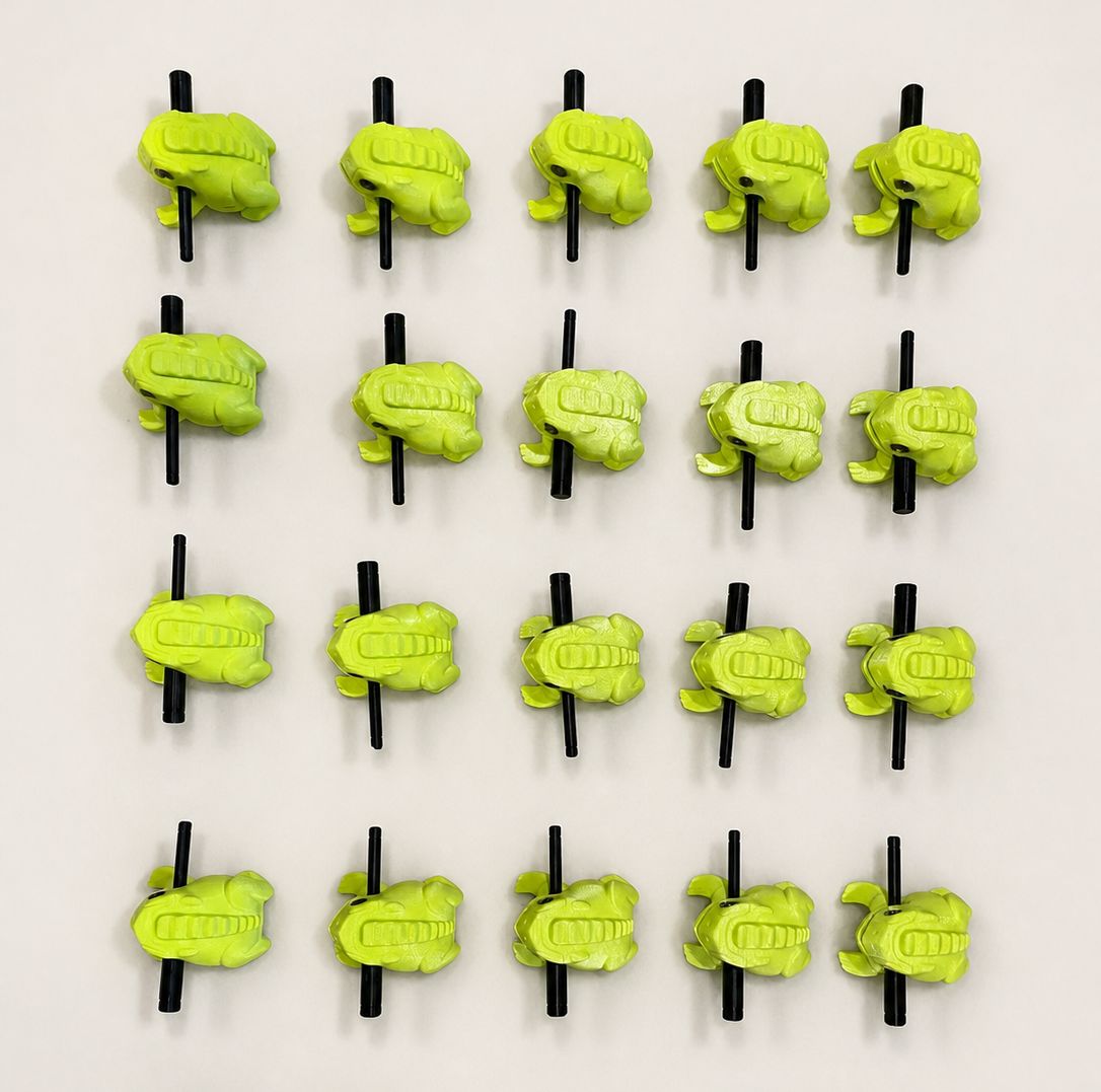 A batch of bright green 3D-printed frog guiros, ready for workshop kits.