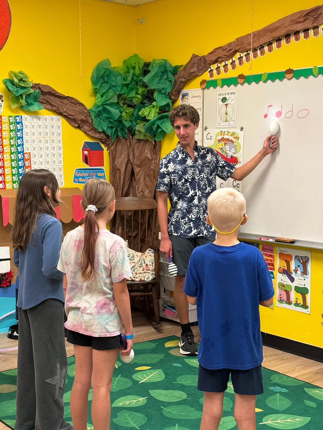 A volunteer points to rhythm notes on a whiteboard as students look on.