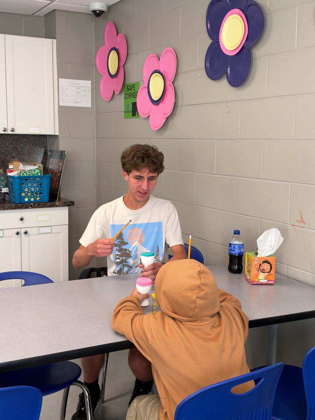 A volunteer works one-on-one with a student, hand drums on the table between them.