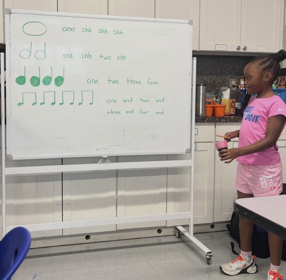 A student plays along to rhythm notation on a whiteboard.