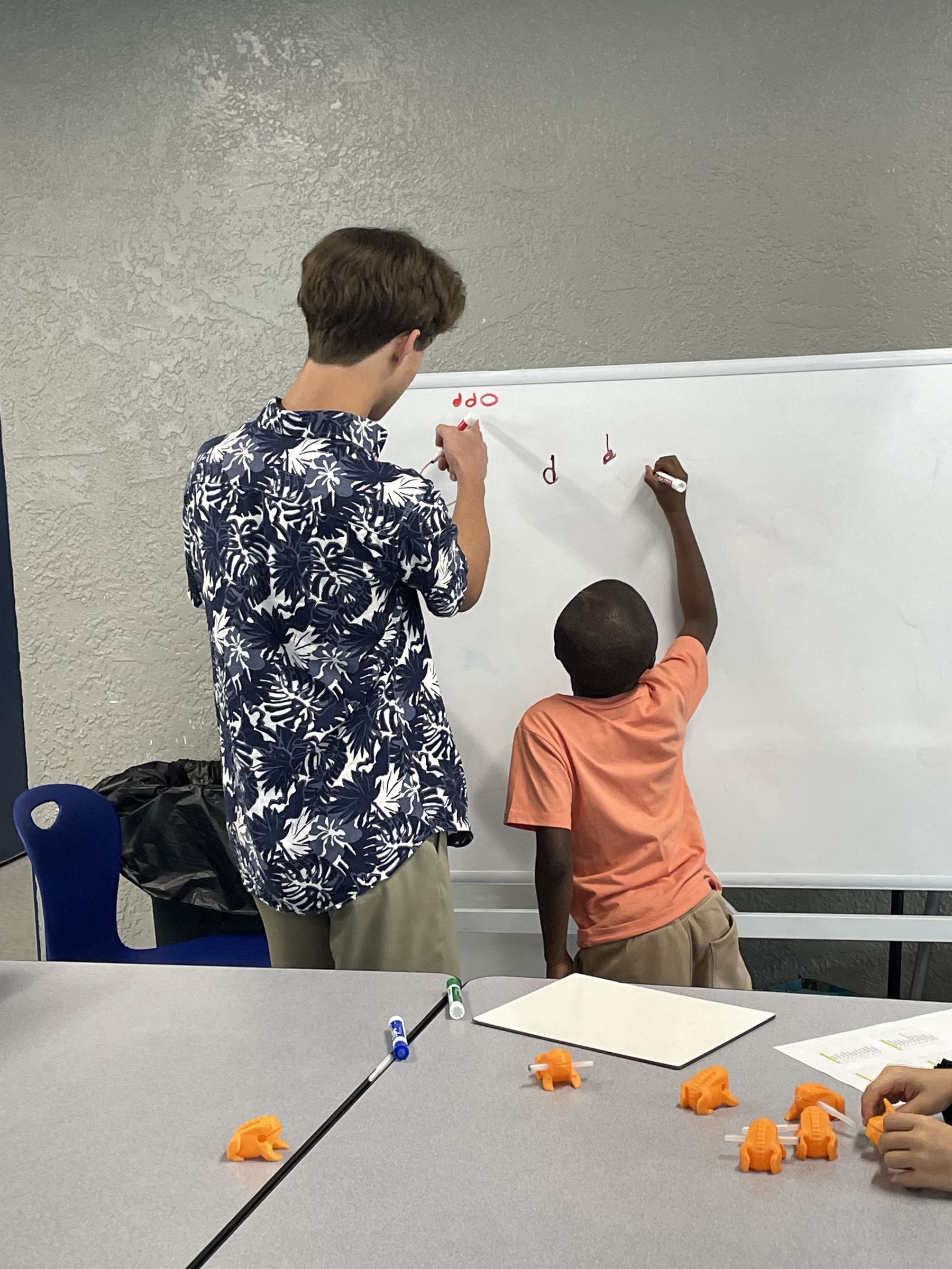 A Print2Play mentor and a young student writing quarter notes together on a whiteboard during a workshop.