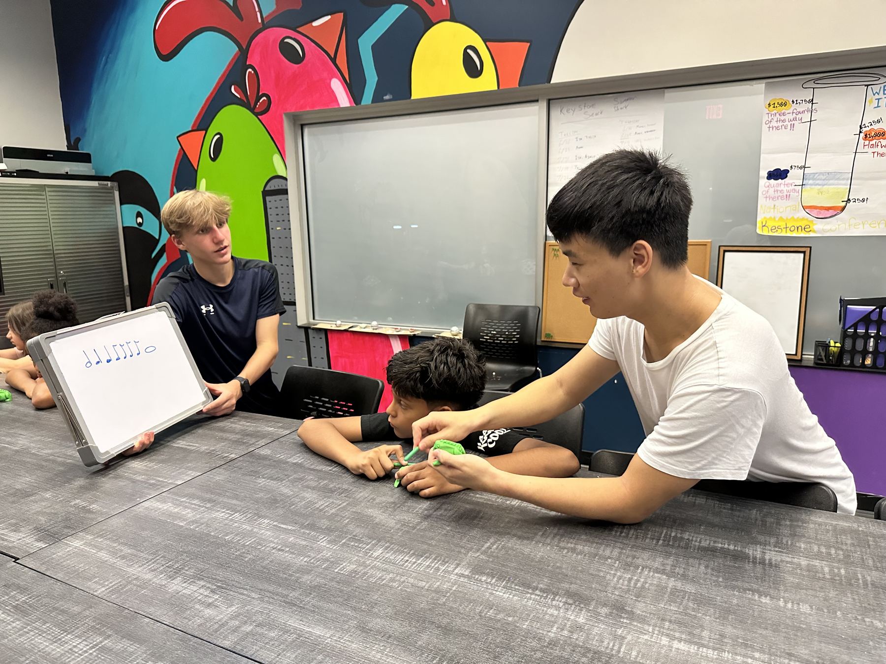 A mentor teaching rhythm notation to a student at a Print2Play workshop table.